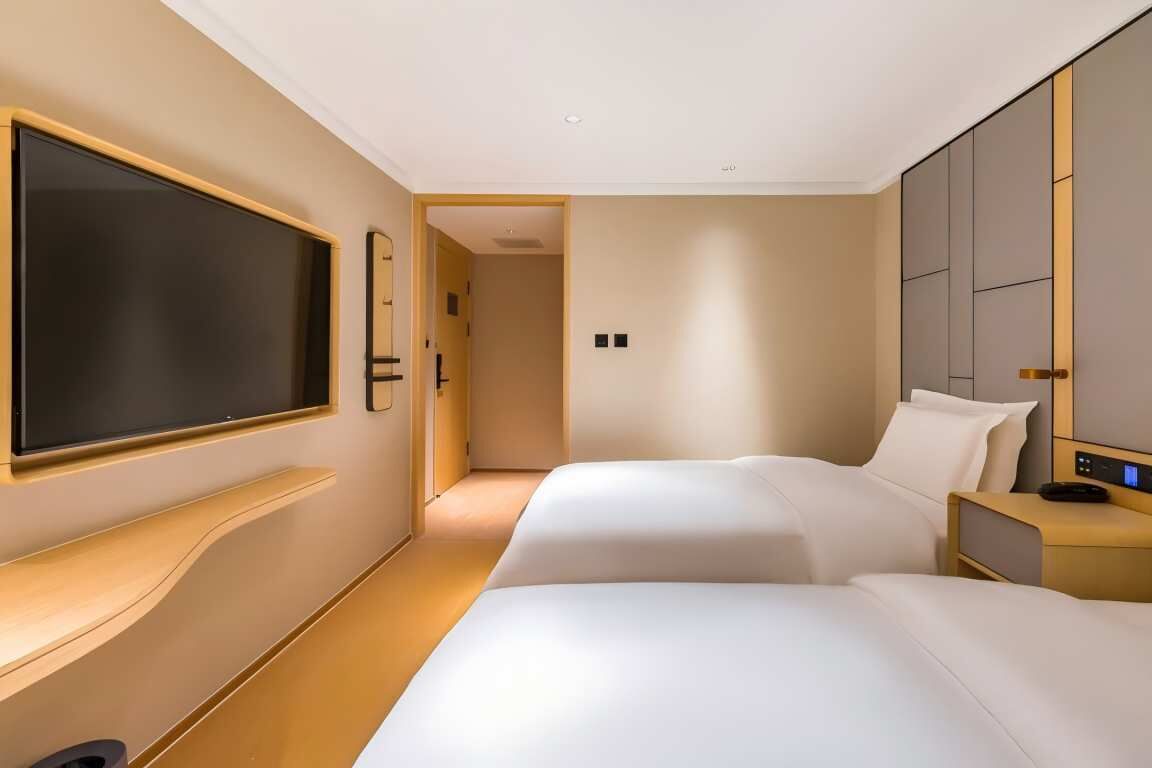 Habitación de hotel con una gran televisión de pantalla plana montada en la pared, cama con ropa de cama blanca, mesita de noche con lámpara y armario con puertas correderas.