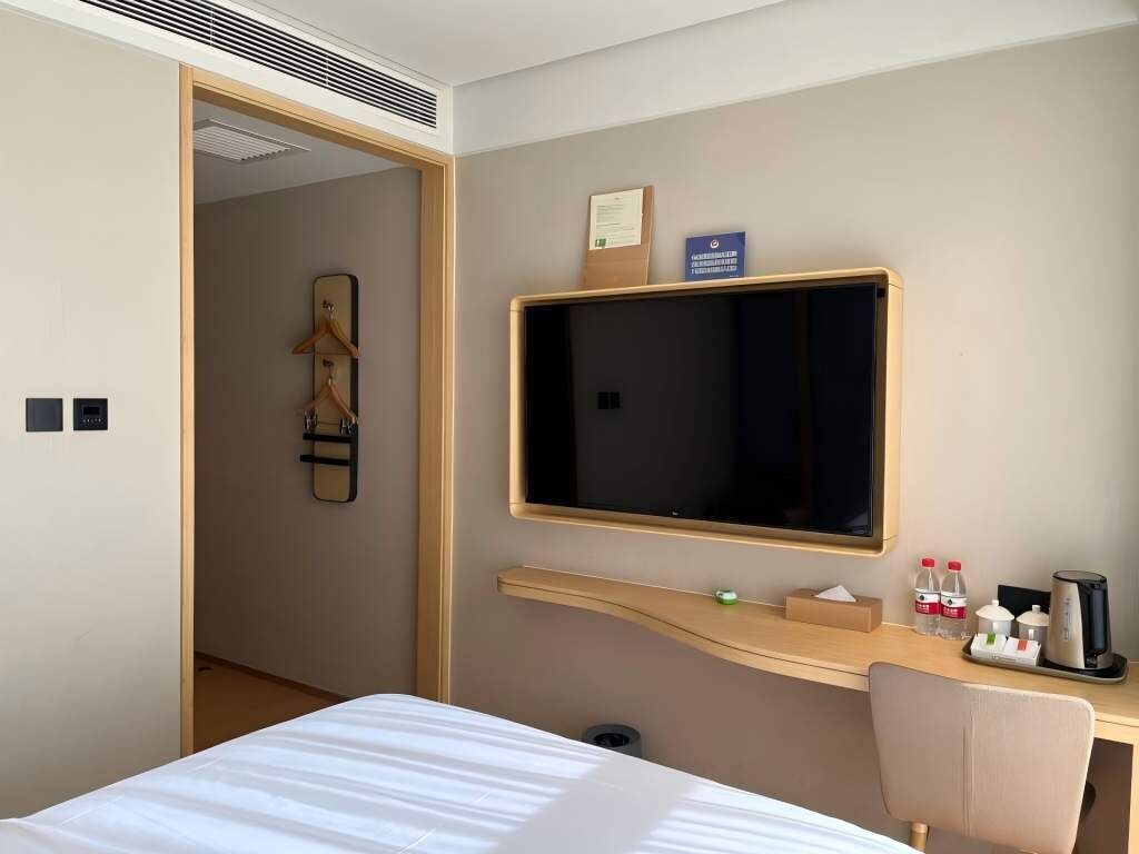 A hotel room with a bed, a desk with a computer, a television, and a coat rack.