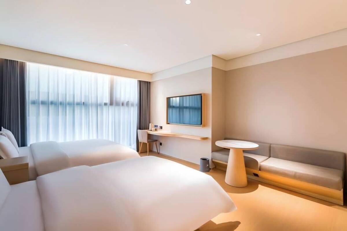 Una habitación de hotel moderna con dos camas grandes, un escritorio pequeño, una mesa redonda y un televisor montado en la pared.