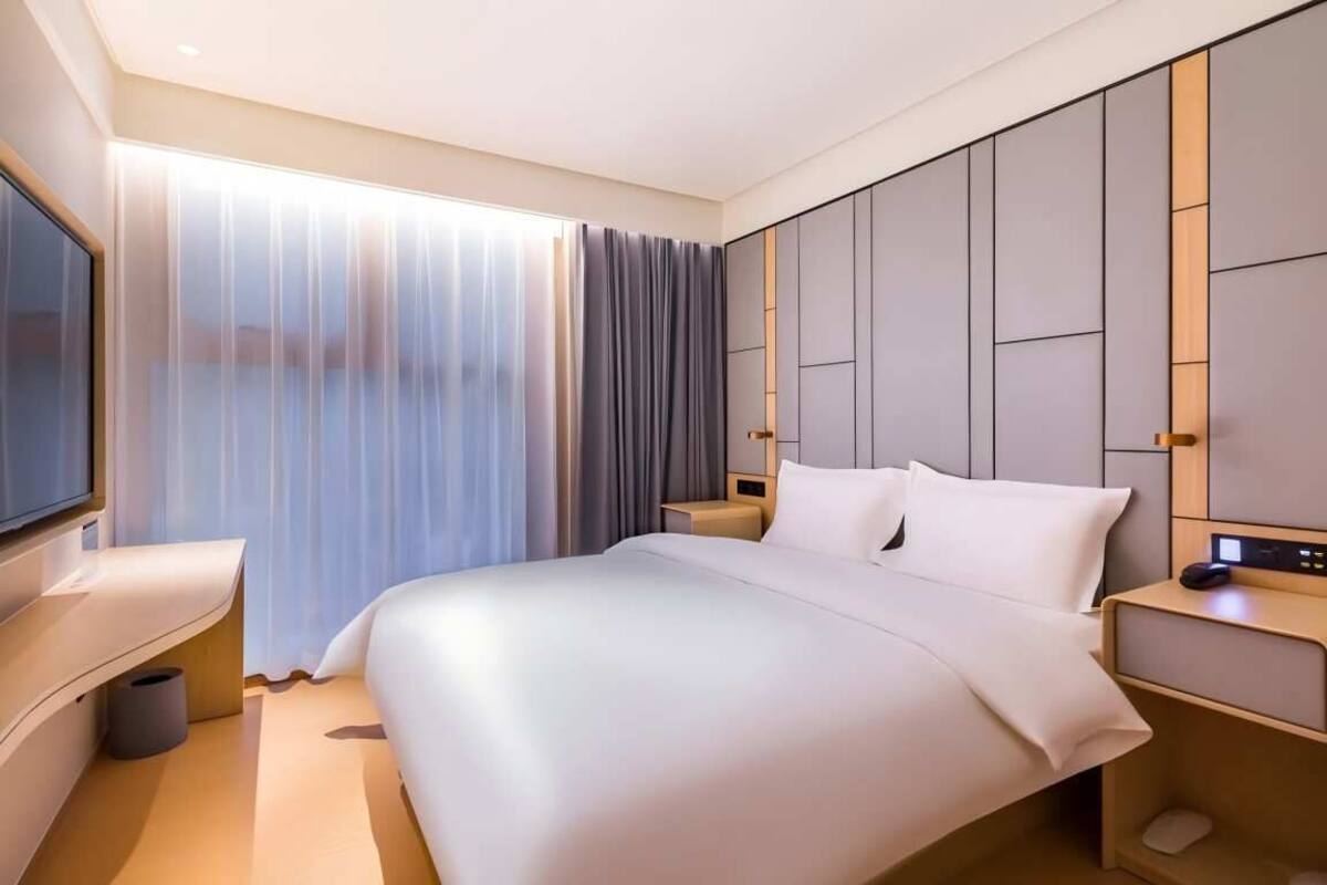 Una habitación de hotel moderna con una cama grande, un televisor, un escritorio y una ventana con cortinas.