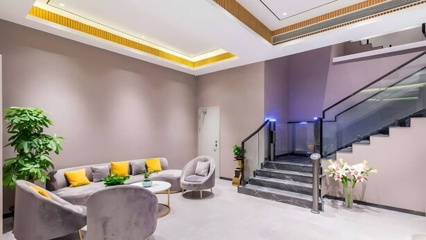 A modern living area with a sofa set, armchairs, and a coffee table. A staircase with glass railings leads to an upper level. - Vienna Classic Hotel (Beijing)