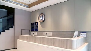 A reception desk with a logo, a staircase, and informational signs. - Vienna Classic Hotel (Beijing)