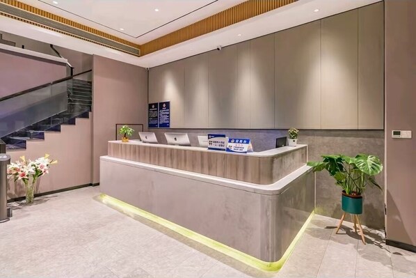 Un moderno mostrador de recepción con una escalera a la izquierda, una planta en maceta a la derecha y un cartel en la pared sobre el mostrador.