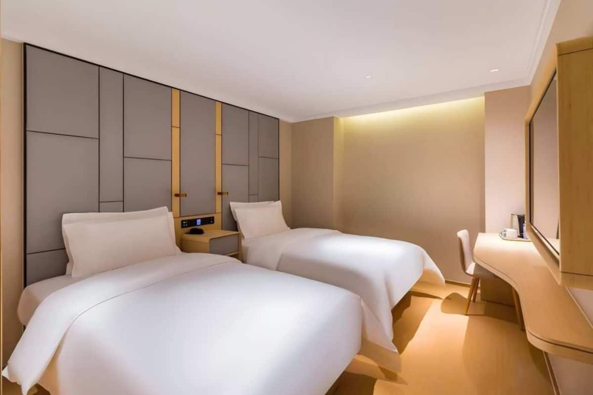Una habitación de hotel moderna con dos camas, una mesita de noche, un escritorio y un espejo grande.