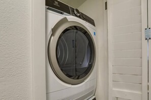 A front-loading washing machine in a laundry room with a white wall and a door with horizontal slats. - Beach Treat!-Luxe Coastal Retreat (Indian Rocks Beach)