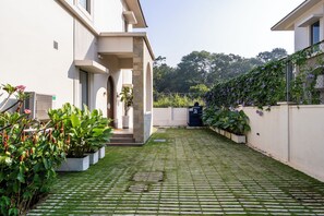 A courtyard with a paved walkway, potted plants, and a building with a white facade. - Staymaster Casa Nivara (Siolim)