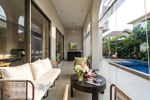 Un espacio interior moderno con un sofá, sillas, una mesa redonda con un florero y vista a una piscina.