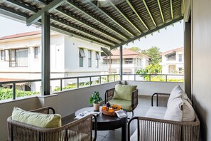 A balcony with wicker furniture, a potted plant, and a table with a tray of fruit and drinks. - Staymaster Casa Nivara (Siolim)
