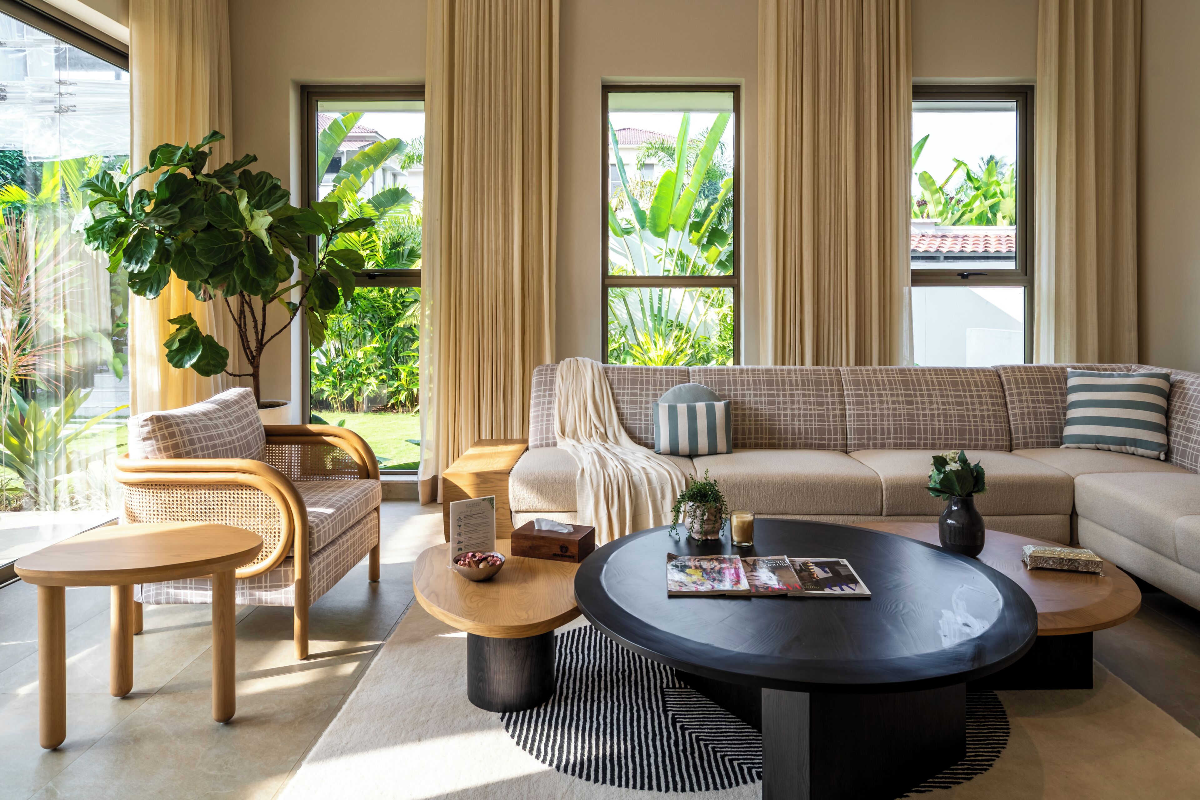 Ein modernes Wohnzimmer mit einer Couch, Sesseln, einem Couchtisch und einem großen Fenster mit Blick auf Grünflächen.