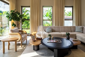 A modern living room with a sofa, chairs, a coffee table, and a large window with a view of greenery. - Staymaster Casa Nivara (Siolim)