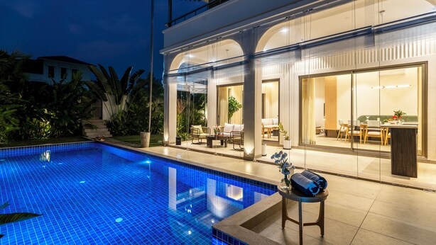 A modern pool area with clear glass walls, a lounge with seating, and a well-lit interior. - Staymaster Casa Nivara (Siolim)