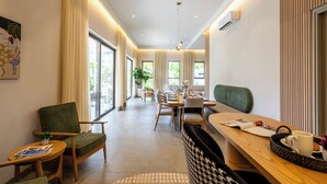 A modern hotel lobby with a dining area, seating, and a large window providing a view of the outdoors. - Staymaster Casa Nivara (Siolim)