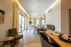 Un moderno vestíbulo de hotel con zona de comedor, asientos y un amplio ventanal con vistas al exterior.