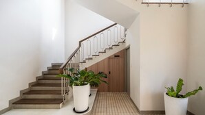 A staircase with a wooden handrail and a white wall. There are two potted plants on the floor. - Staymaster Casa Nivara (Siolim)
