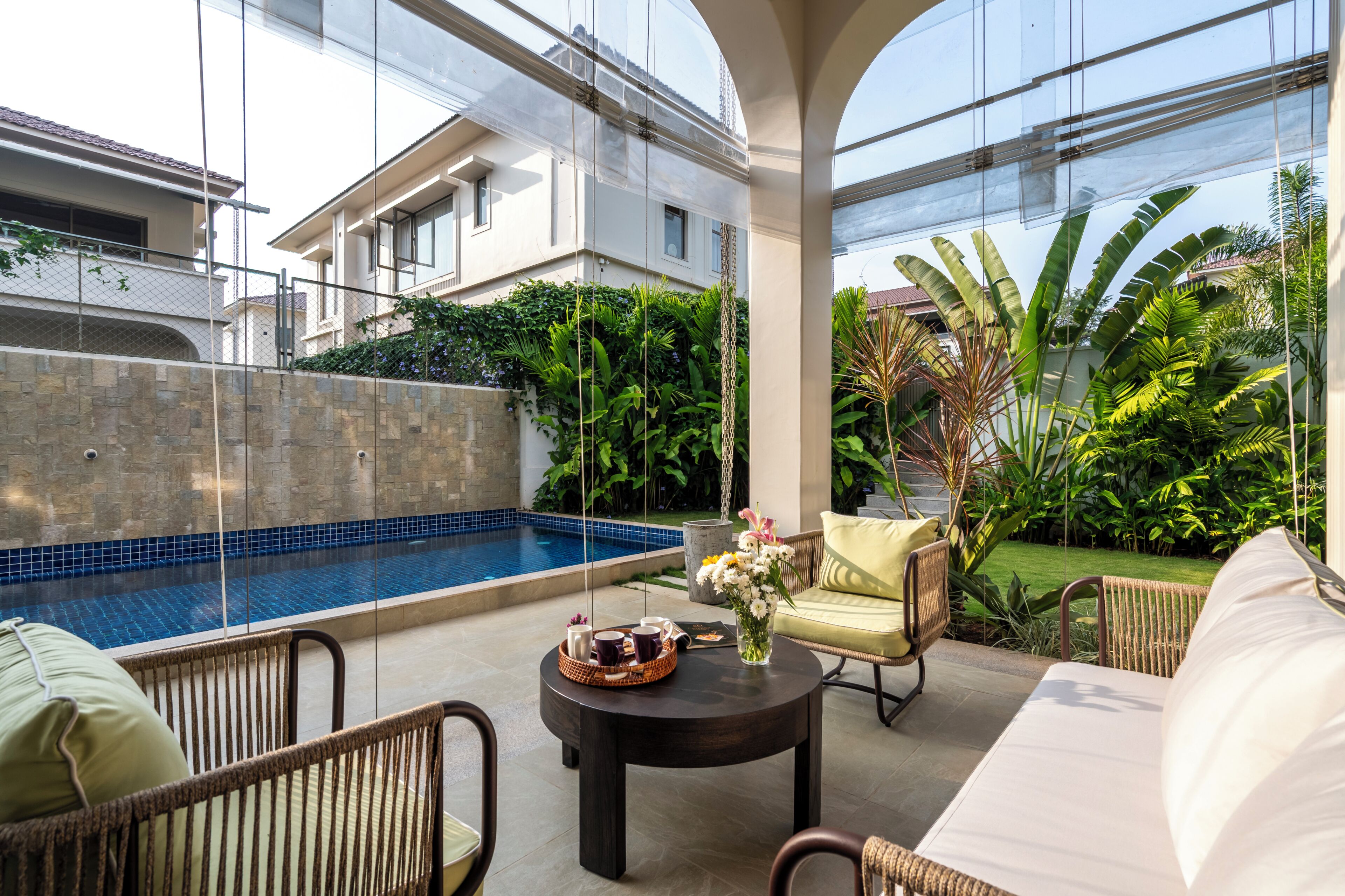 Uma área de estar moderna ao ar livre com piscina, móveis de vime e vista para um jardim exuberante.