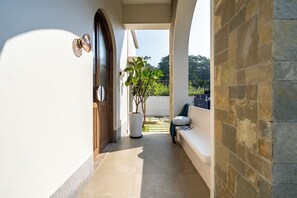 A corridor with a wooden door, a potted plant, a bench, and a stone wall. - Staymaster Casa Nivara (Siolim)