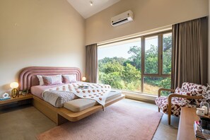 Un dormitorio con cama, mesita de noche, lámpara y vistas a la vegetación por la ventana.