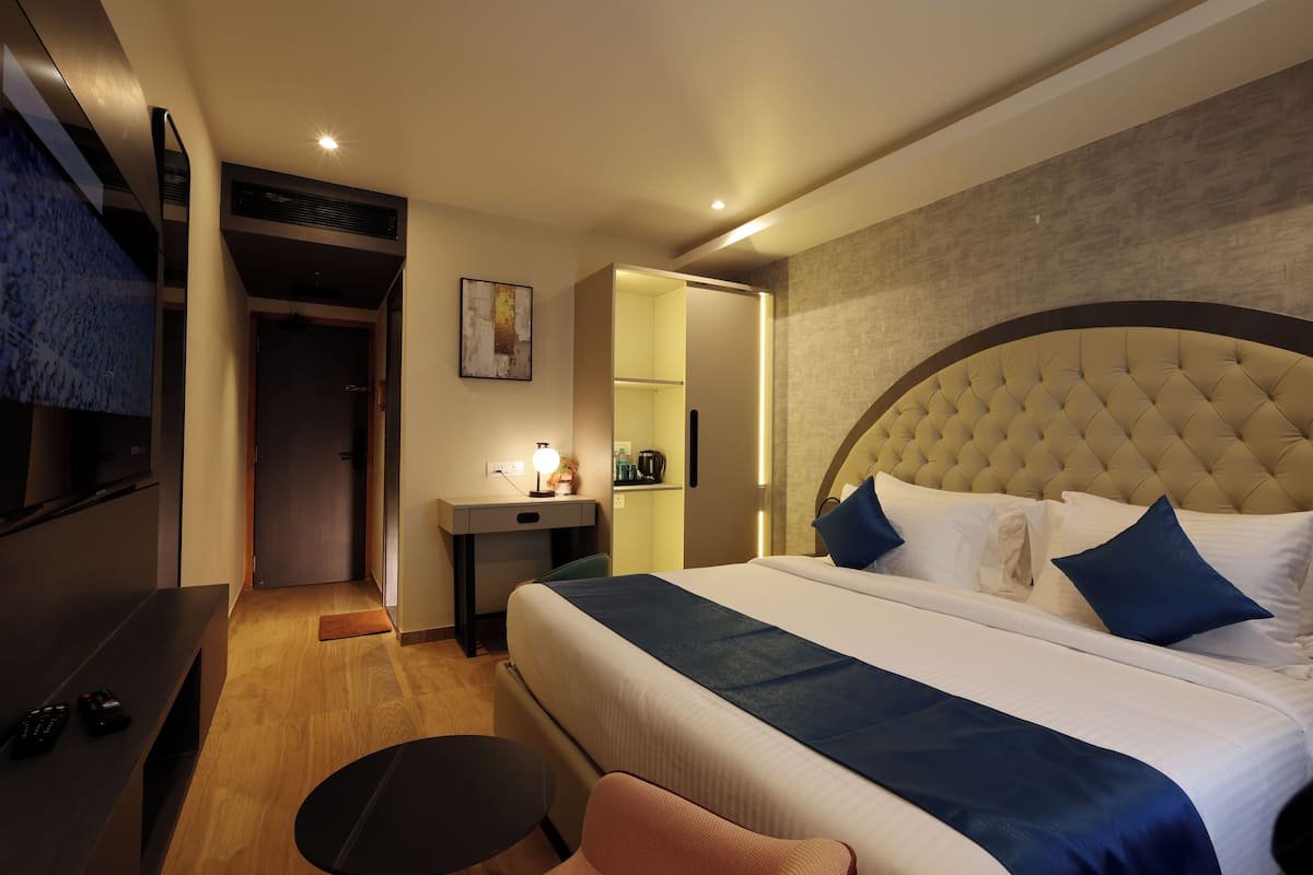 A hotel room with a bed, a desk, a chair, a TV, and a door.