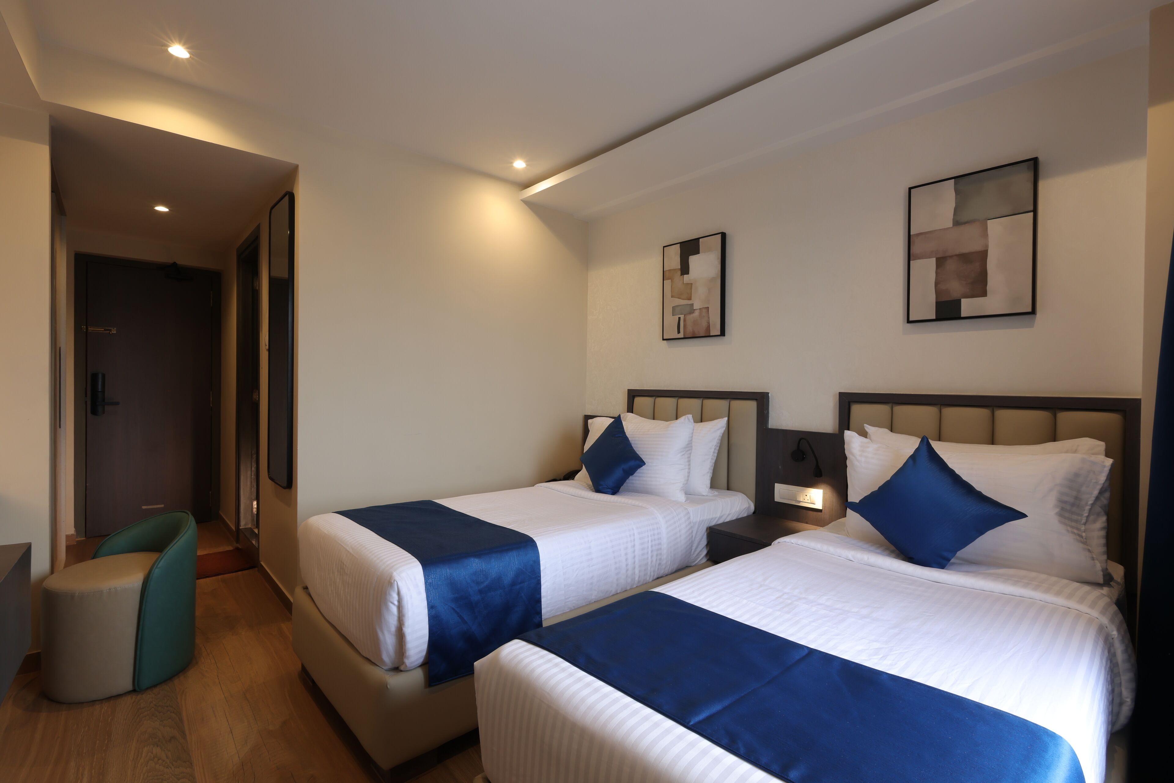 Une chambre d’hôtel avec deux lits, un bureau, une chaise et des œuvres d’art accrochées aux murs.