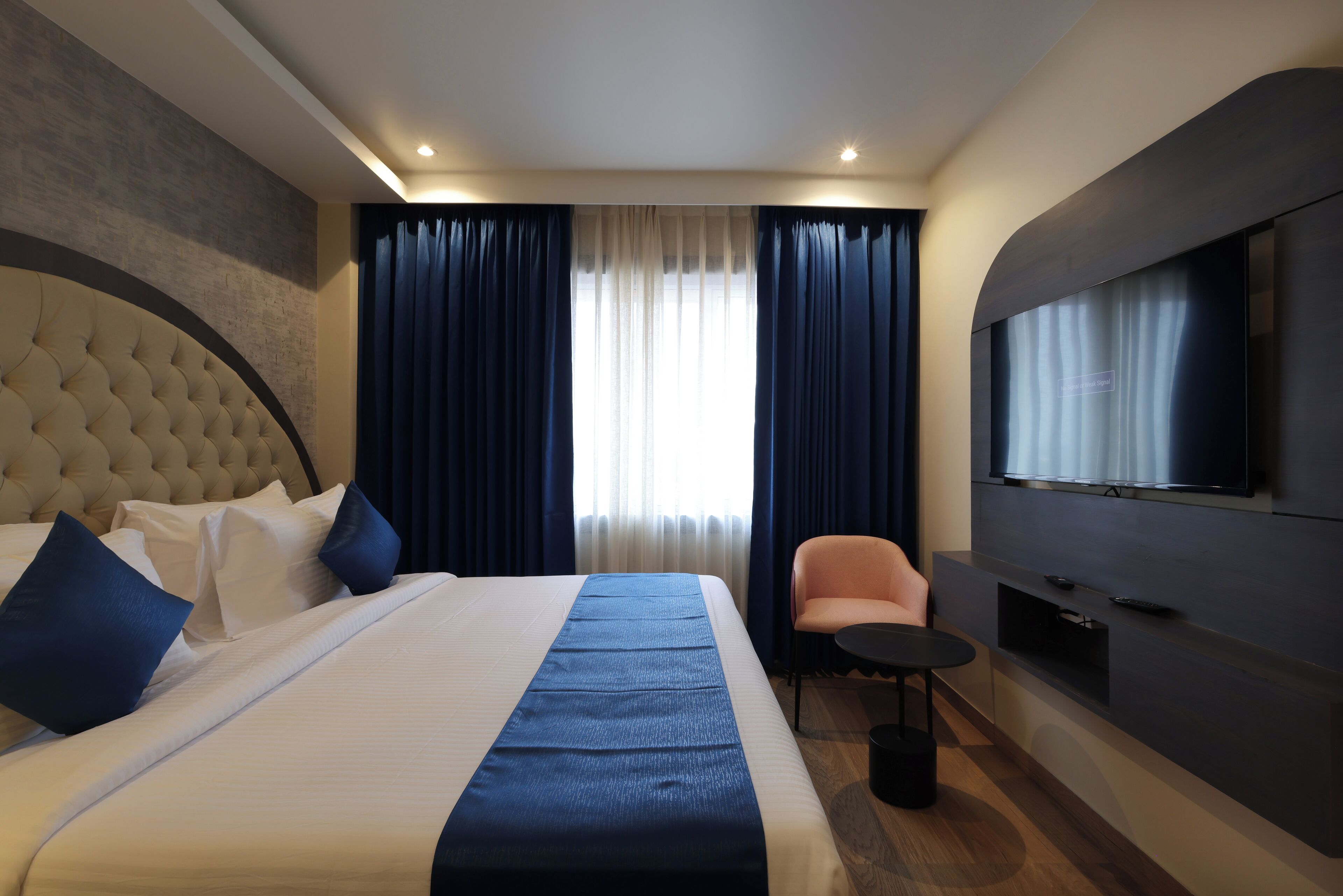 Habitación de hotel con una cama grande, televisión, zona de estar y ventana con cortinas.