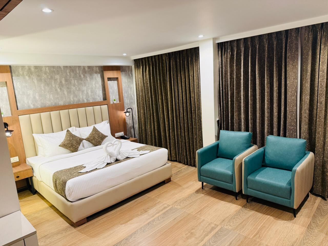 Una habitación de hotel con una cama grande, dos sillones, un cabecero de madera y una cortina.
