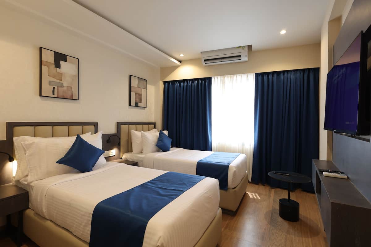 A hotel room with two beds, a flat-screen TV, a desk, and a window with curtains.