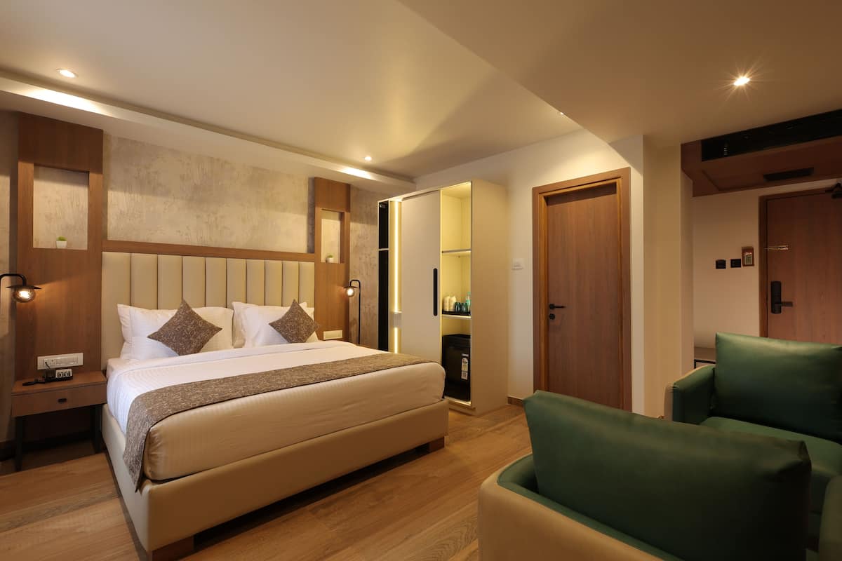 A hotel room with a bed, bedside tables, a green armchair, and a wardrobe.
