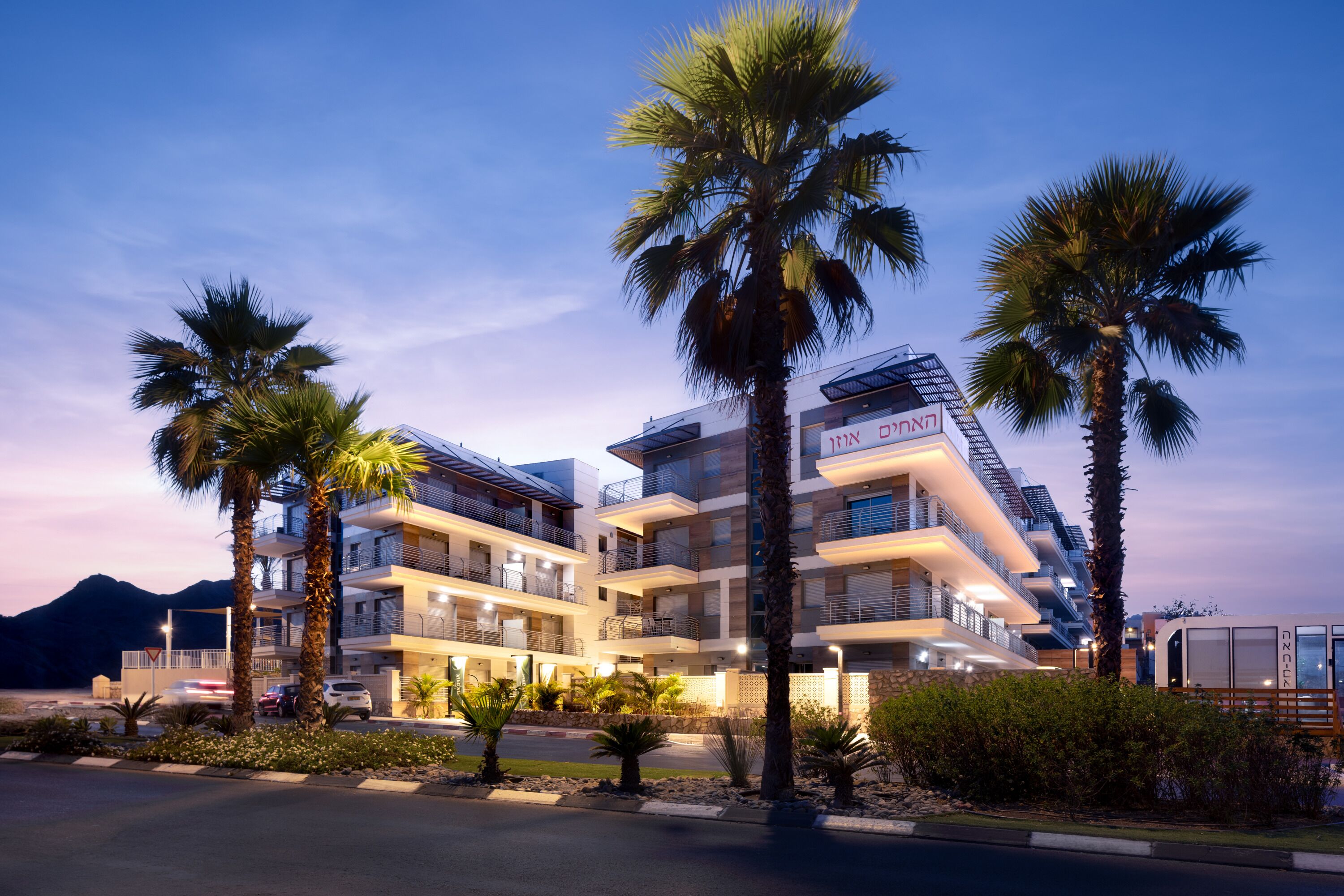 A multi-story hotel with balconies, palm trees, and a mountain in the background.