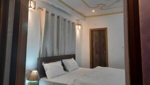 Een slaapkamer met een bed, nachtkastje, lamp, raam met gordijnen en een deur.
