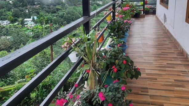 Een houten balkon met potplanten en bloemen, met uitzicht op een weelderige groene vallei in de mist.