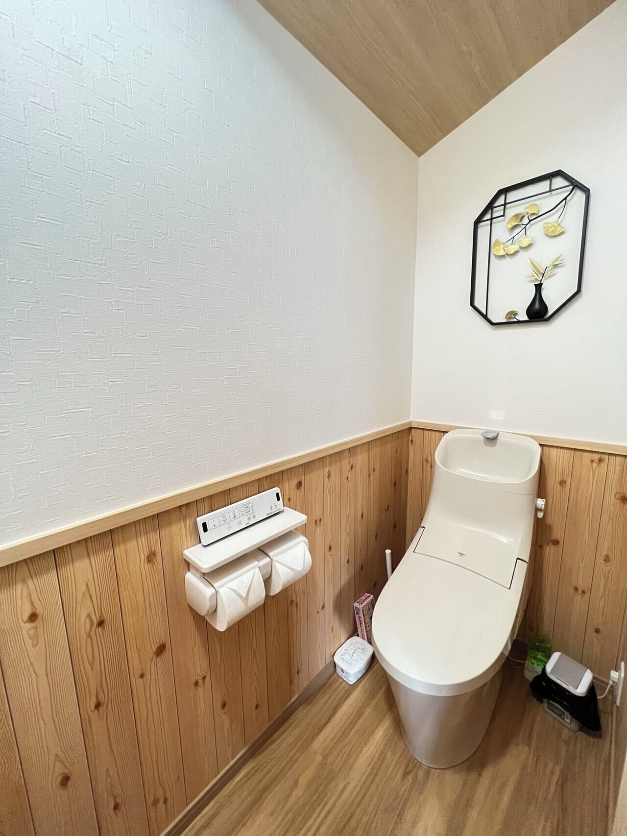 A modern bathroom with a wooden panel wall, a white toilet, a small sink, and a towel rack with a power strip.