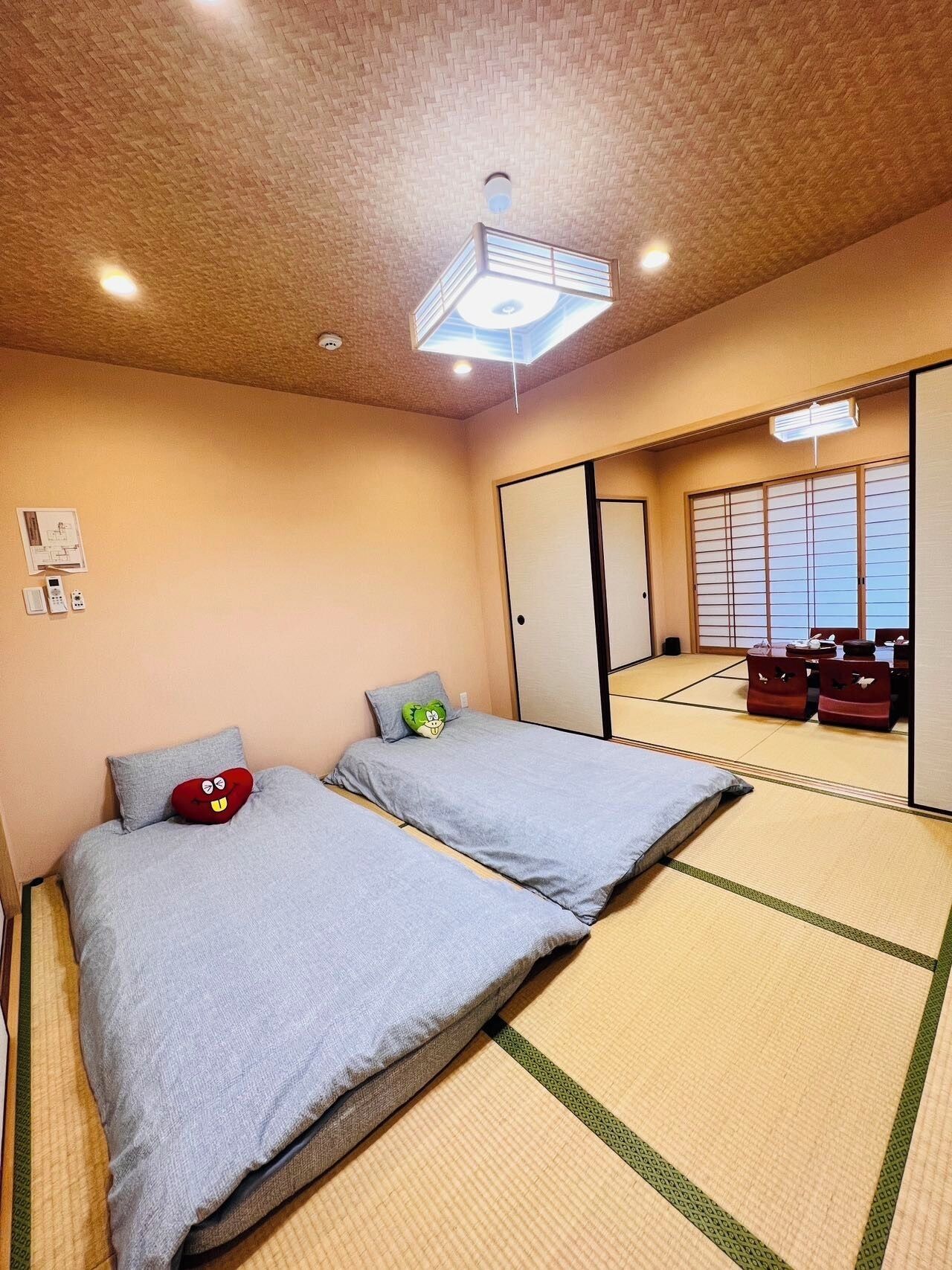 Een kamer met twee bedden, tatami matten, een plafondventilator en een schuifdeur die leidt tot een traditionele Japanse kamer.