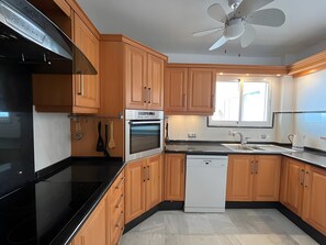 Una cocina moderna con gabinetes de madera, estufa negra, horno, lavavajillas y ventilador de techo.