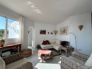 Una sala de estar con sofá, reposapiés, muebles de mimbre, un cuadro y una lámpara.