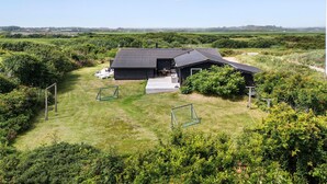 Une maison moderne dotée d’une grande terrasse, entourée d’une végétation luxuriante et surplombant un ciel dégagé.