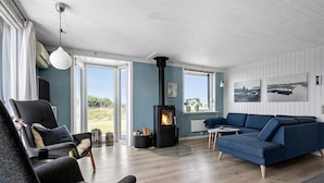 Un salon moderne avec un poêle à bois, un canapé bleu et une grande fenêtre donnant sur l’extérieur.