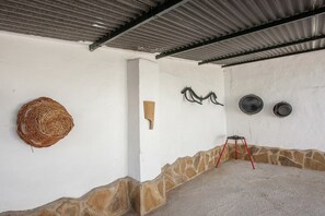 Ein Zimmer mit Wellblechdach, einem gewebten Korb an der Wand, einer Sockel aus Stein und einem roten Ständer mit zwei schwarzen Schüsseln.