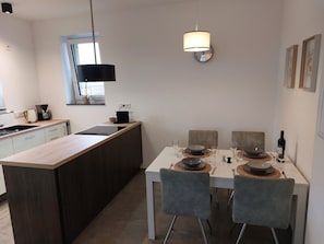 Una cocina moderna con una isla central, una mesa de comedor para cuatro personas y una lámpara colgante arriba.