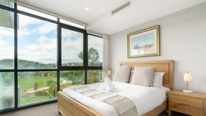 A bedroom with a large window, a wooden bed, a nightstand, and a framed picture on the wall. - Premium Apartment with Scenic Views near City (Campbell)