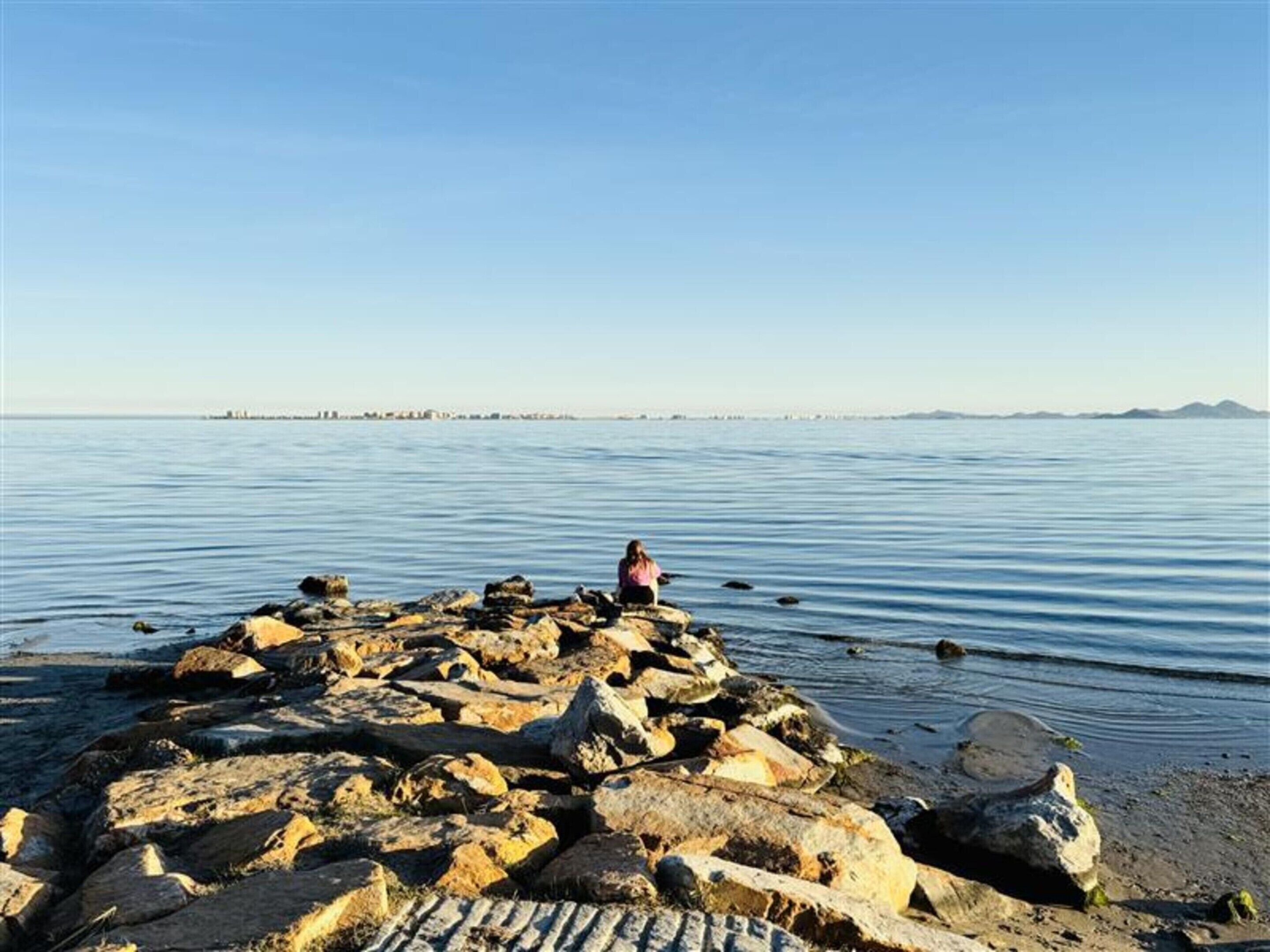 A rocky shoreline with a person sitting on the rocks.