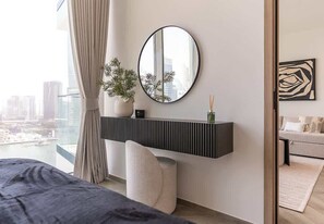 Une chambre moderne avec un grand lit, une table de chevet agrémentée d’un vase et d’une plante, un miroir rond accroché au mur et une vue sur la ville.