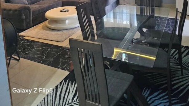 Ein modernes Wohnzimmer mit einem Glastisch, grauem Sofa und einer Chandelüster.