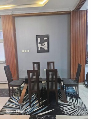 A dining area with a table and chairs, a patterned rug, and a framed picture on the wall.