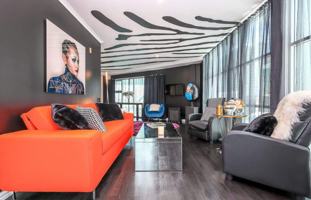 A modern living room with a zebra-striped ceiling, a large window with curtains, and a sofa with a fluffy pillow.