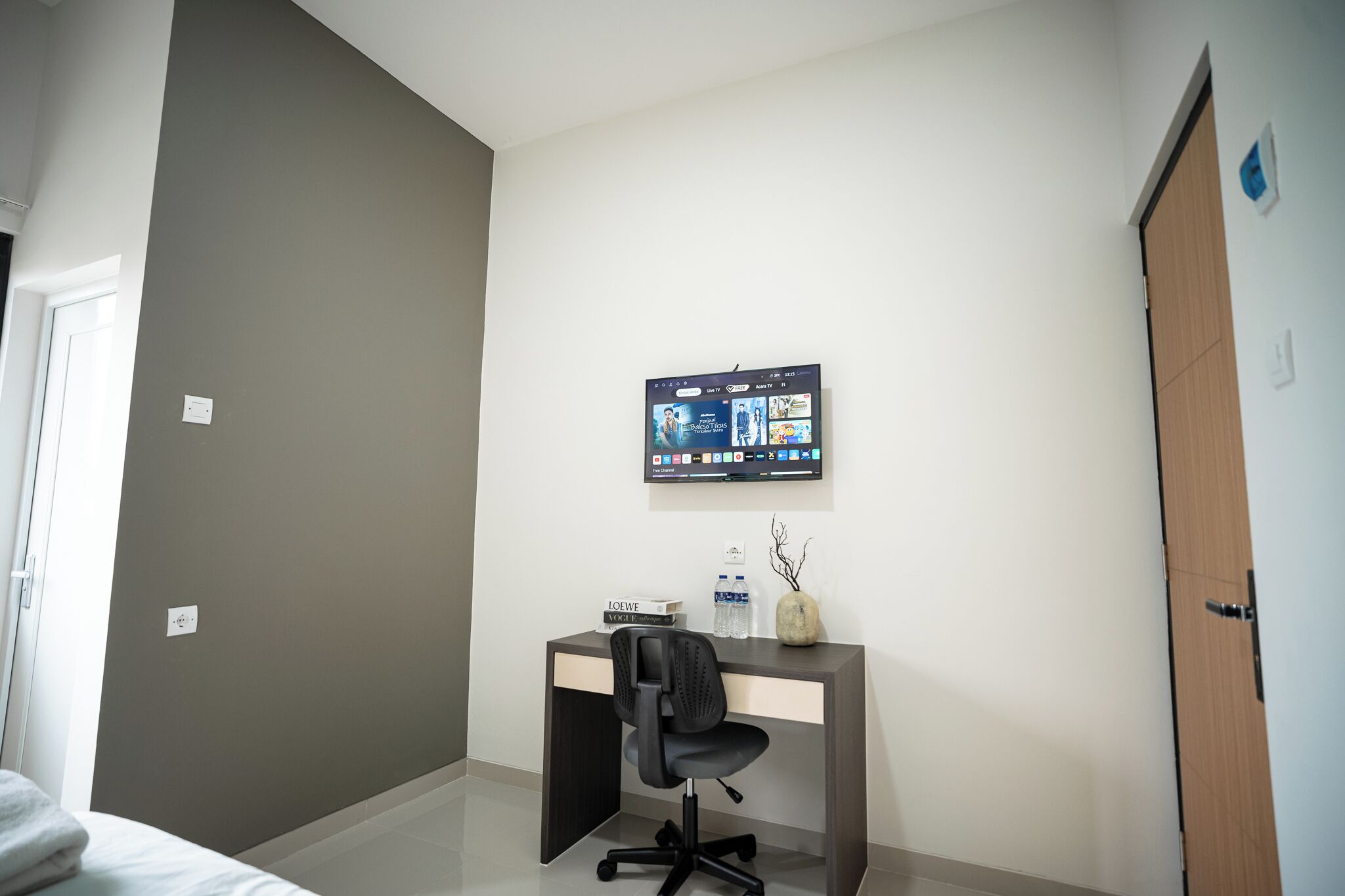 A hotel room with a desk, chair, and a mounted TV displaying a streaming service interface.