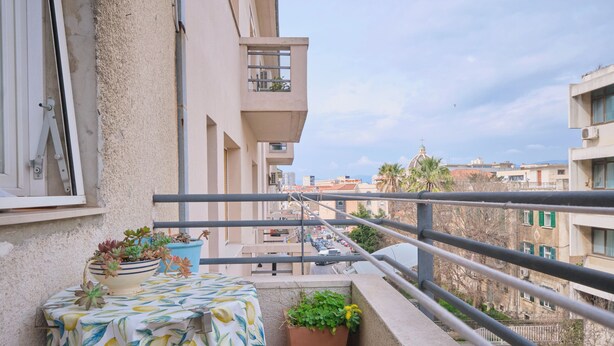 Un balcón con una mesa, plantas en macetas y barandilla con vistas a la ciudad.