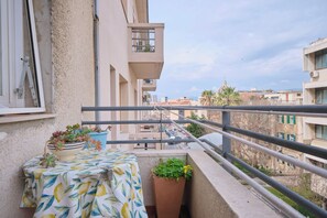 Un balcon avec une table, des plantes en pot et une balustrade donnant sur un paysage urbain.