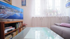 Una sala de estar con televisor de pantalla plana, estantería, mesa de centro de vidrio y sofá.
