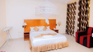 Quarto de hotel com cama, mesa de cabeceira, luminária, cadeira e cortina.