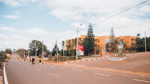 Uma estrada com um ciclista, um edifício com uma placa e árvores.